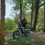 Rider in helmet standing with Buzymoto DAT70 blue electric dirt bike in forest setting
