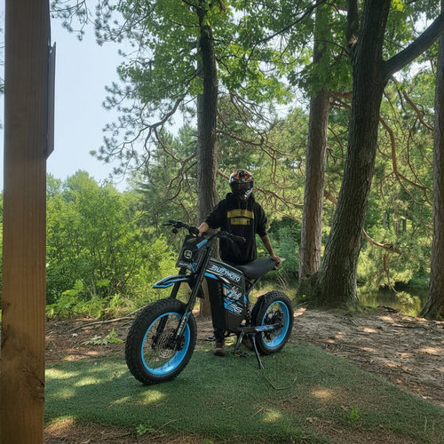 Rider in helmet standing with Buzymoto DAT70 blue electric dirt bike in forest setting