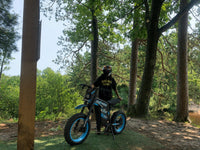 Rider exploring a forest trail on a blue Buzymoto electric dirt bike from Dirt Bike Mall