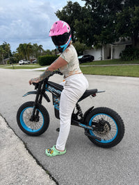 Rider wearing a pink helmet on a blue Buzymoto electric dirt bike on the street
