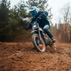 Rider in helmet cornering Buzymoto DAT70 orange electric dirt bike on dirt trail in forest