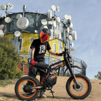 Rider in helmet posing with Buzymoto DAT70 orange electric dirt bike in front of urban graffiti wall
