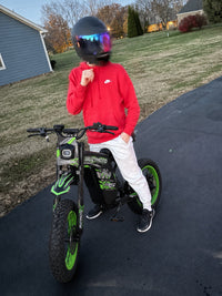 Rider in a red hoodie riding a green Buzymoto electric dirt bike from Dirt Bike Mall