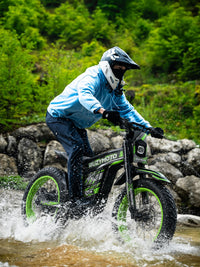 Green Buzymoto electric dirt bike riding through a shallow water crossing