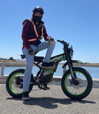 Rider on a green Buzymoto electric dirt bike beside the waterfront