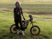 Young rider on an orange Buzymoto electric dirt bike in an open field