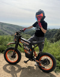 Rider exploring a mountain trail on an orange Buzymoto electric dirt bike