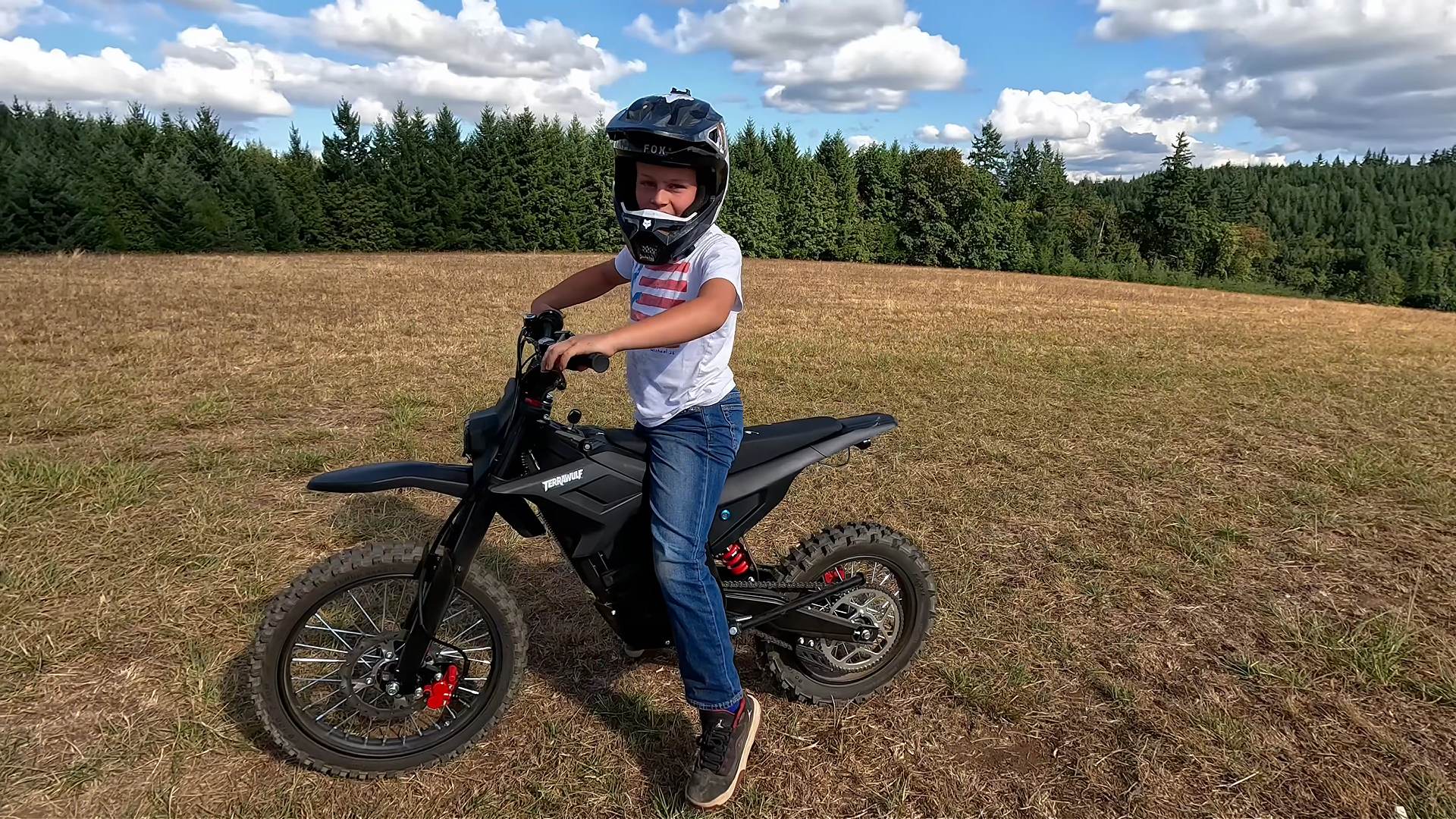 Young rider sitting on a Terrawulf M7 electric dirt bike in an open field
