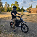 Adult rider in helmet straddling Terrawulf M7 black electric dirt bike on gravel road at sunset