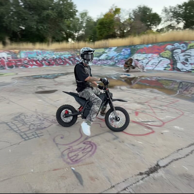 Rider in helmet riding Terrawulf M7 black electric dirt bike inside a graffiti-covered skatepark