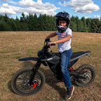 Young rider in Fox helmet posing with Terrawulf M7 black electric dirt bike in open field