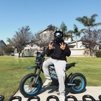 Rider posing with Buzymoto DAT70 blue electric dirt bike outdoors on grass