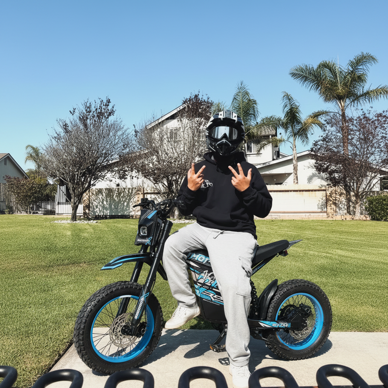 Rider posing with Buzymoto DAT70 blue electric dirt bike outdoors on grass